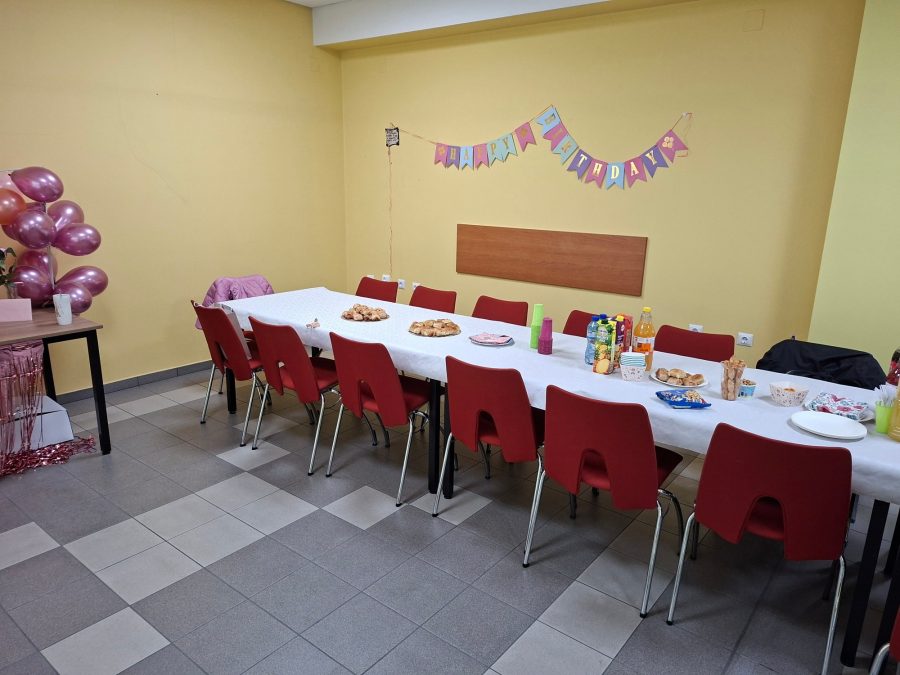 Маса за възрастни с червени столове, хапки и напитки под гирлянд Happy Birthday