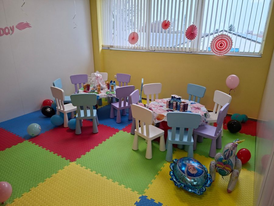Същите детски маси от друг ъгъл, с розови розети на прозореца и балони-единорог на пода