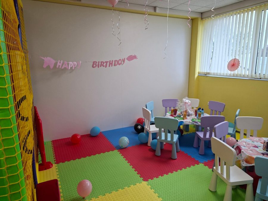 Розов надпис Happy Birthday на стената над детските маси, до мрежата на игралната конструкция