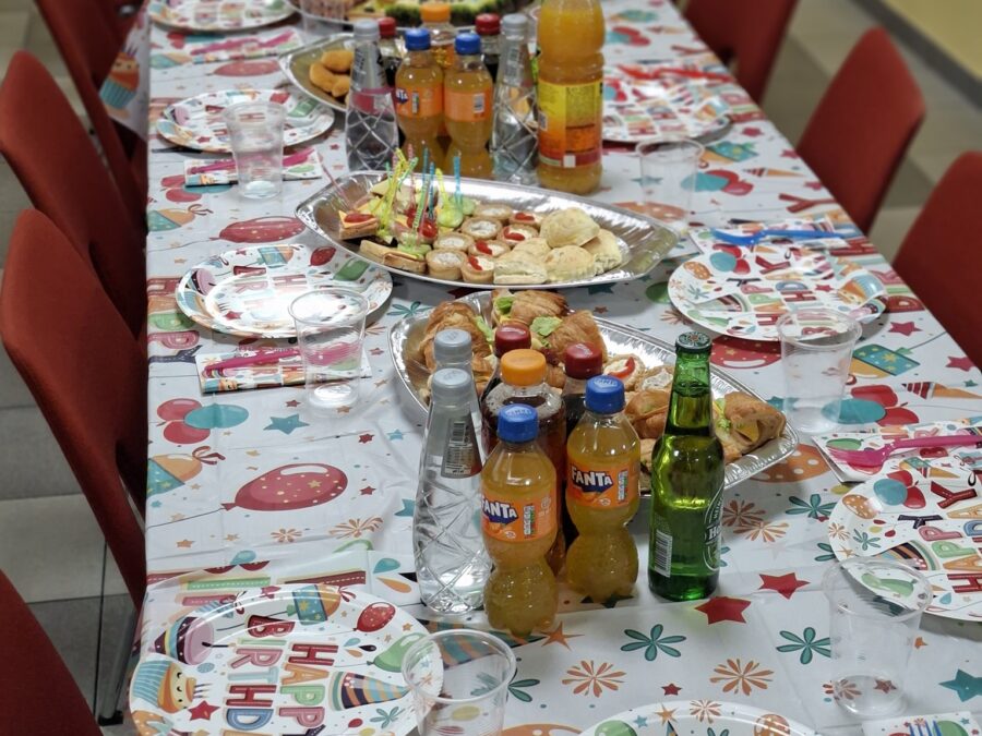 Дълга маса с червени столове, отрупана със сандвичи, Fanta и чинии Happy Birthday