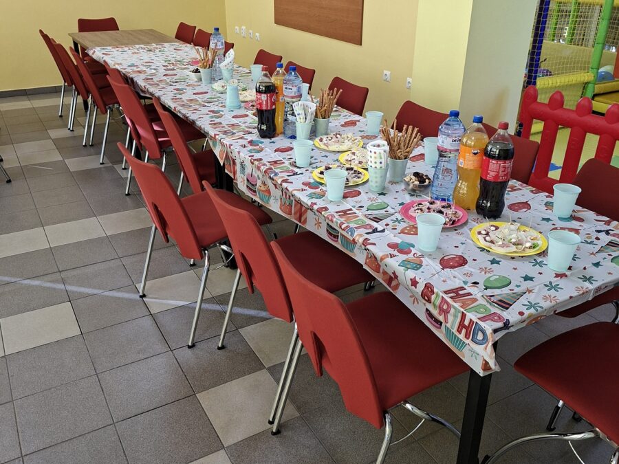 Детската маса с шарени чинии и прибори, а зад нея балон Happy Birthday до площадката