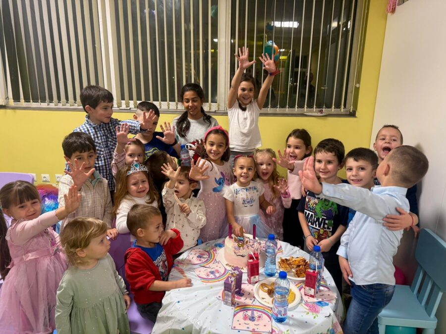 Децата вдигат ръце и махат весело край масата с тортата преди рязането