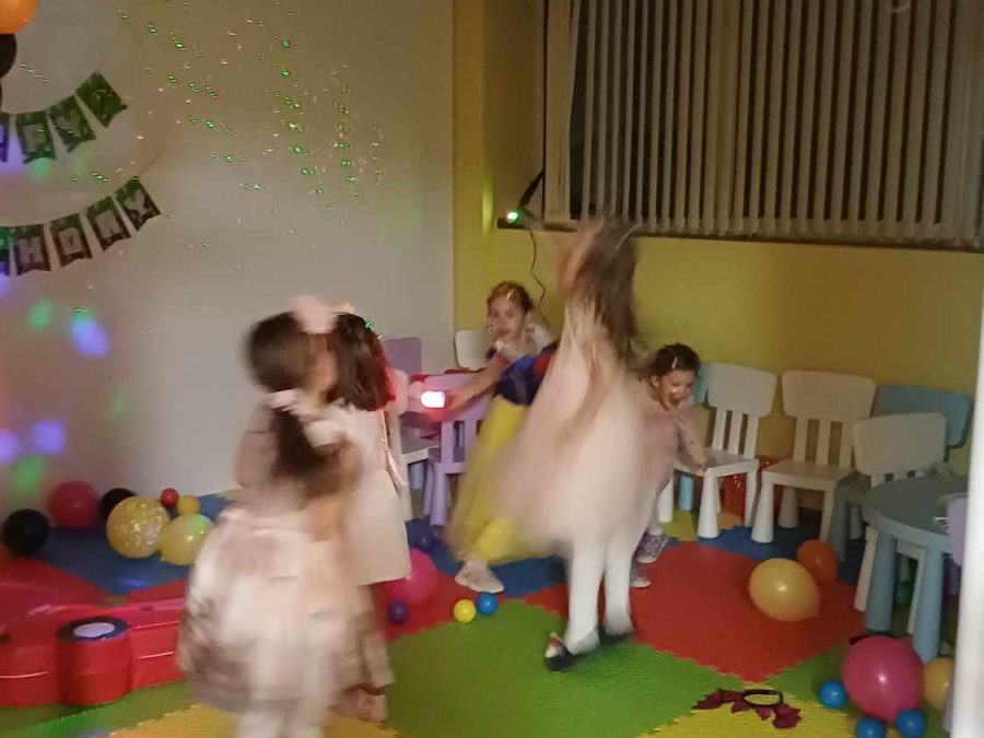 Деца в рокли танцуват на цветна ЕВА настилка под балони и пано Happy Birthday, с диско светлини