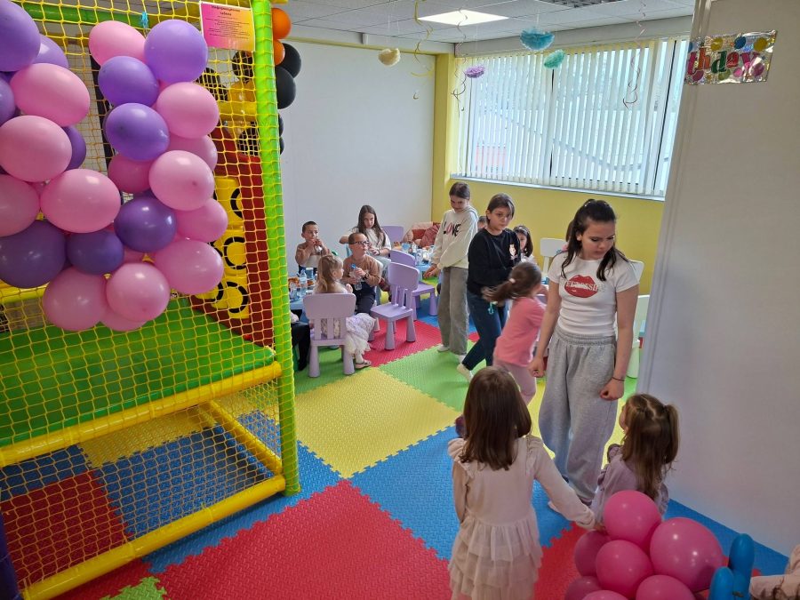 Деца и родители играят край цветна игрална конструкция с розово-лилав балонен стълб