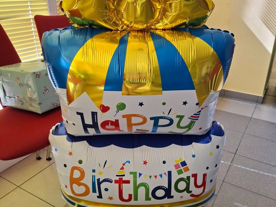 Златен фолиев балон с форма на подарък и надписи Happy Birthday, поставен до прозореца